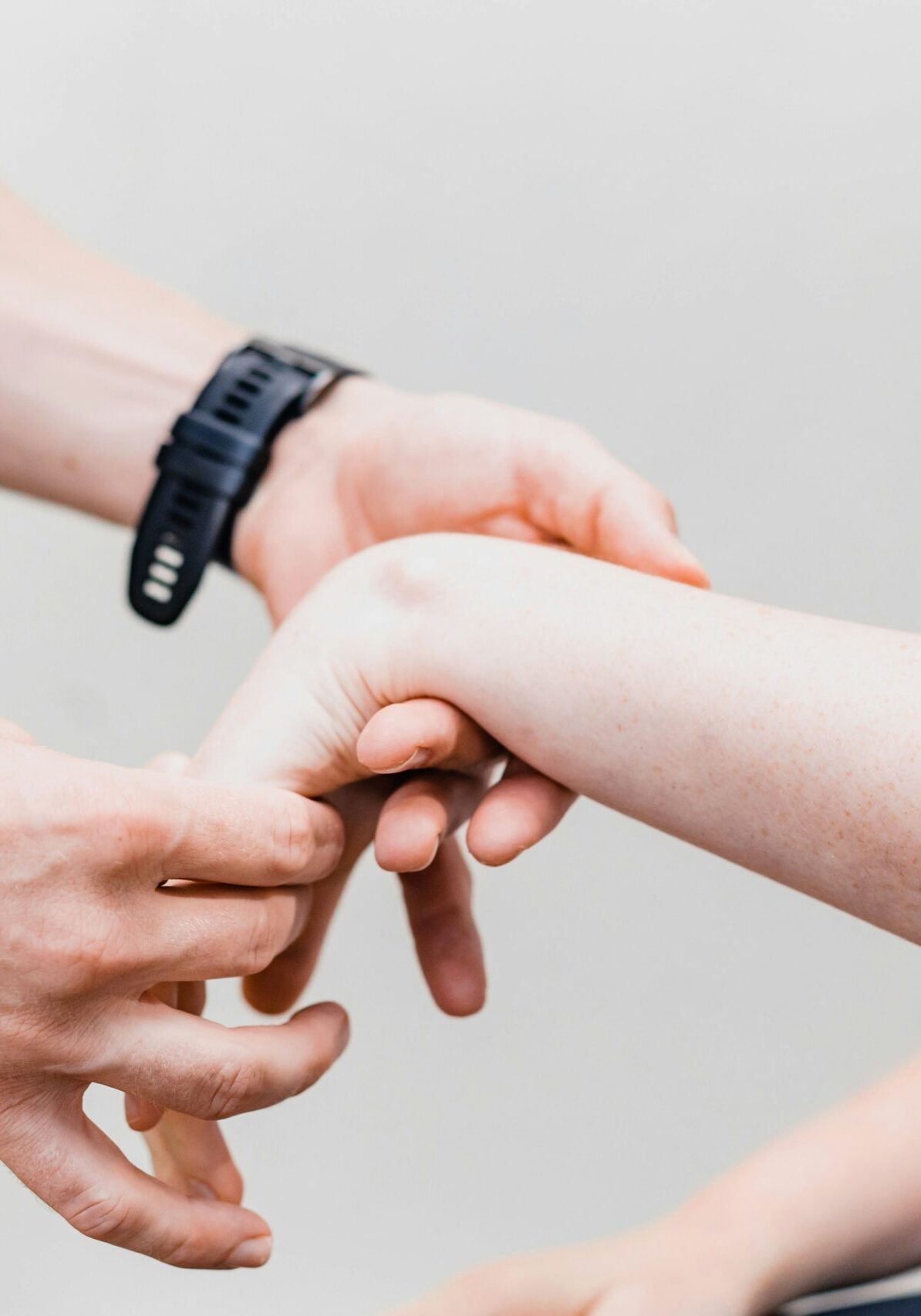 Close-up of multiple hands joining in a teamwork gesture, with one wrist wearing a black band watch, against a light background.